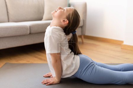 Photo for Glad cute millennial caucasian teenager girl in sportswear doing stretching workout, practicing yoga in living room interior, close up. Sports, fitness and health care at home - Royalty Free Image
