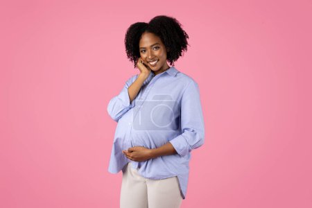 Foto de Positivo millennial africano americano rizado embarazada dama tocar gran vientre con la mano, pensar, aislado en rosa fondo del estudio. Mamá disfruta esperando bebé, cuidado de la salud, maternidad, anuncio, oferta - Imagen libre de derechos