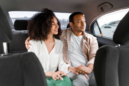 Foto de Confort del viaje en taxi. Marido y esposa árabes contentos sentados en el asiento trasero en un auto de lujo, mirando por la ventana. Pasajeros que viajan en automóvil cómodo, vista desde el panel frontal - Imagen libre de derechos