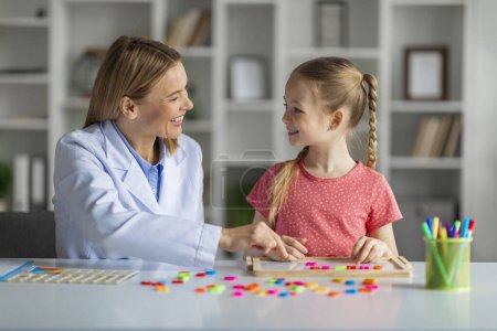 Photo for Child Development School. Professional woman language teacher exercising with little girl, cute female child making word with colorful letters on table, enjoying session with speech therapist - Royalty Free Image