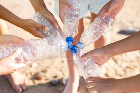 Téléchargez les photos : Des adolescents et des jeunes multiraciaux tiennent des bouteilles en plastique sur la plage en été, recadrées, rapprochées, avec vue sur le dessus. Protection de l'environnement, recyclage, éco-économie et nettoyage ensemble, travail d'équipe - en image libre de droit