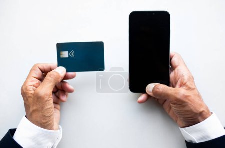 Téléchargez les photos : Homme européen mature utilise carte de crédit et smartphone avec écran vide sur table blanche, vue de dessus, recadré. App, site web, gadget pour les entreprises à distance, paiement et banque en ligne - en image libre de droit