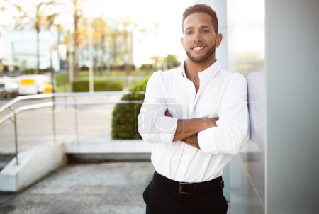 Photo for Successful male entrepreneur. Outdoors portrait of european businessman standing near modern office building and posing at camera with folded arms - Royalty Free Image