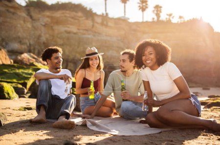 Foto de Alegre millennial multiracial personas estudiante con botellas disfrutar de vacaciones de verano, picnic, divertirse en la playa, al aire libre. Fiesta juntos, estilo de vida, tiempo libre y fin de semana con bebida - Imagen libre de derechos
