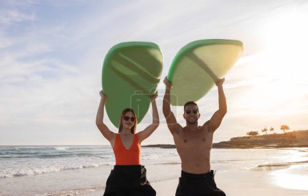 Foto de Retrato de hermosa pareja joven surfeando juntos en la playa, surfistas milenarios hombre y mujer sosteniendo tablas de surf por encima de las cabezas y sonriendo en la cámara, disfrutando de un estilo de vida activo, Copiar el espacio - Imagen libre de derechos