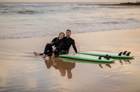 Photo for Surf Date. Young Beautiful Couple Relaxing On The Beach After Surfing Together, Romantic Millennial Man And Woman Sitting On Sand Near Their Surfboards And Embracing, Chilling On Seashore - Royalty Free Image