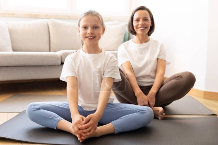 Photo for Positive millennial caucasian woman in sportswear and teenage daughter practice yoga, training at mat in living room interior. Sports at home, body care and health care together - Royalty Free Image