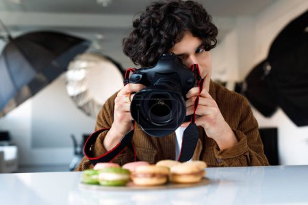 Photo for Food photographer caucasian man taking photos of delicious sweets macarons at photo studio, using digital camera and professional lighting equipment - Royalty Free Image