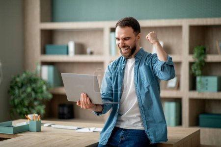 Photo for Business Success. Young Happy Businessman Celebrating Success With Laptop In Office, Overjoyed Male Entrepreneur Shaking Fist And Shouting Yes, Standing With Computer Near Desk Indoors, Copy Space - Royalty Free Image
