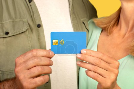 Photo for Cropped closeup view of unrecognizable middle aged couple holding credit card on yellow studio background. Man and woman promoting contactless shopping - Royalty Free Image