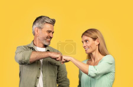 Photo for Teamwork concept. Happy middle aged man and woman bumping fists and smiling, celebrating success partnership triumph standing on yellow studio background - Royalty Free Image