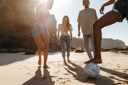 Foto de Feliz millennial diversas personas estudiantes jugando pelota de fútbol, disfrutar de vacaciones de verano, divertirse en la playa, al aire libre, recortado. Deporte, estilo de vida activo, tiempo libre en fin de semana y juego juntos - Imagen libre de derechos
