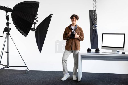 Photo for Happy european male photographer with dslr camera posing in his own modern photostudio, looking at camera and smiling, standing ready for work, full length, free space - Royalty Free Image