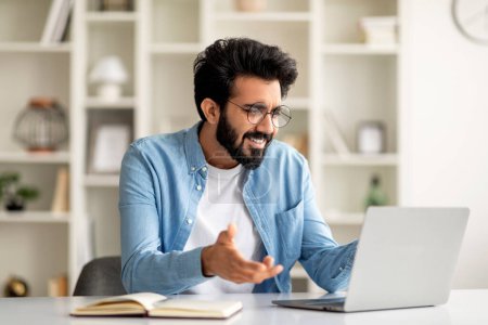Photo for Unexpected News. Confused Indian Male Freelancer Looking At Laptop Screen And Smiling, Cheerful Young Eastern Male Wearing Eyeglasses Reading Email While Sitting At Desk In Home Office, Copy Space - Royalty Free Image