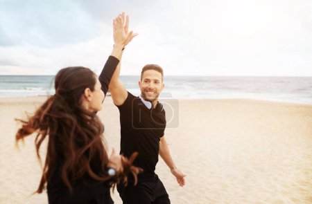 Téléchargez les photos : Bonjour Jogging ensemble. Un homme et une femme souriants courent et donnent cinq sur la plage près de l'océan le matin. Jeune couple européen de coureurs profitant de l'entraînement de jogging en plein air. Soins de santé et sport - en image libre de droit