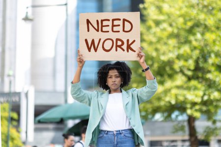 Photo for Determined jobless attractive young black woman wearing smart casual outfit holding need work board placard, standing on the street. Unemployment for millennials, crisis - Royalty Free Image