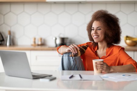 Photo for Black Freelancer Lady Using Laptop While Eating Breakfast In Kitchen, Happy African American Female Having Coffee With Croissant And Watching Videos On Computer At Home, Copy Space - Royalty Free Image