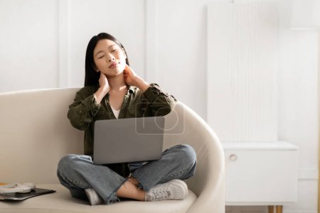 Photo for Office syndrome. Tired exhausted young asian woman wearing casual outfit independent contractor sitting on couch with computer pc laptop on her lap, massaging her neck, home interior, copy space - Royalty Free Image
