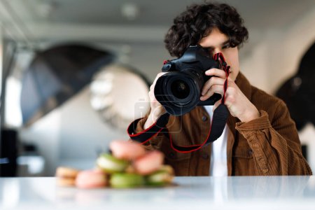 Photo for Man blogger taking photos of sweets macarons for his blog, using professional camera and other equipment for photoshoot, copy space. Blogging concept - Royalty Free Image