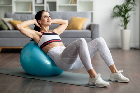 Photo for Athletic well-fit sporty young woman wearing tight sportswear doing exercises with fit ball at home, working on abs muscles, doing crunches, copy space. Fitness tools for home workout - Royalty Free Image