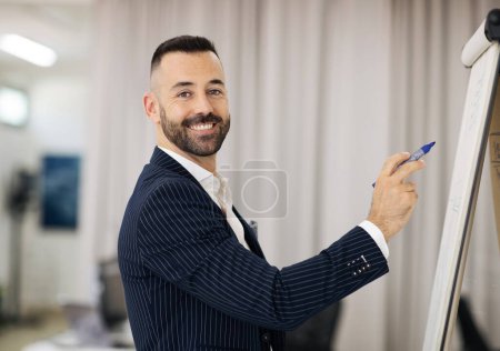 Photo for Happy handsome european adult man in suit with beard teacher writing on blackboard in office coworking interior. Successful business study, webinar, work and professional occupation - Royalty Free Image