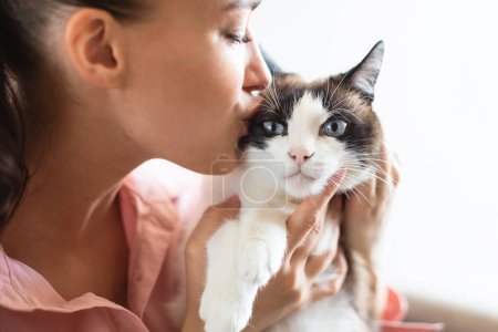 Photo for Pet love. European young lady kissing her cute cat with blue eyes, closeup over white studio background. Selective focus. Best fluffy friend care, domestic animal ownership and adoption - Royalty Free Image