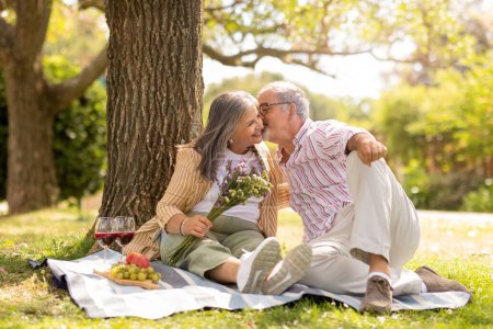 Photo for Smiling old european husband gives bouquet of flowers to wife, kiss, enjoy picnic together in park, celebrate birthday anniversary outdoor. Holiday, romantic date, weekend and free time - Royalty Free Image