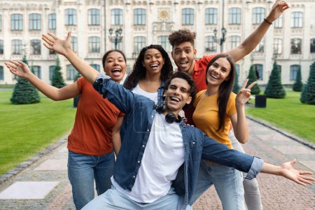 Téléchargez les photos : Photo de groupe. Portrait d'étudiants multiculturels joyeux posant en plein air près de l'immeuble du collège, amis multiethniques positifs s'amusant ensemble à l'extérieur, levant les mains et riant, regardant la caméra - en image libre de droit