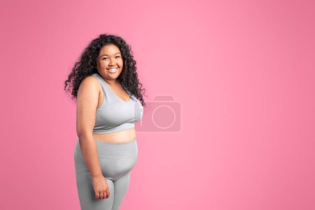 Téléchargez les photos : Portrait de femme noire positive dans le soutien-gorge haut de sport et leggings posant et souriant à la caméra isolée sur fond de studio rose, bannière, espace libre - en image libre de droit
