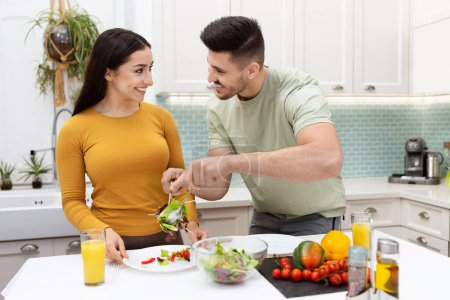 Photo for Happy cheerful loving beautiful young couple handsome man and pretty long-haired woman have healthy dinner together at home, eating fresh vegetable salad, drinking orange juice, copy space - Royalty Free Image