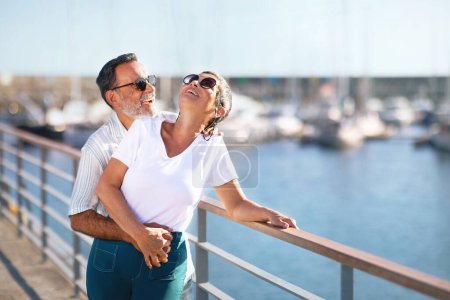 Téléchargez les photos : Summer Love Story. Couple sénior romantique embrassant exprimant le bonheur debout à Marina Pier à l'extérieur, souriant et riant de joie le jour d'été au bord de la mer. Vacances en mer à un âge plus avancé. Espace libre - en image libre de droit