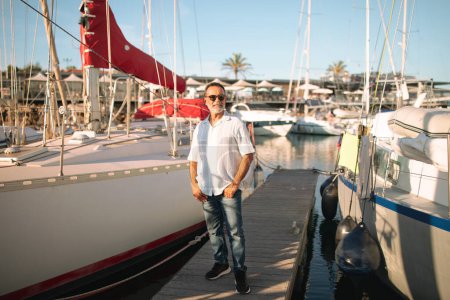 Photo for Yacht Owner. Tanned Mature Man On Vacation Posing Near Luxury Sailboat Outdoor, Standing With Confidence At Marina Boats Park Outside, Full Lengt Shot. Summer Tourism And Seaside Life Concept - Royalty Free Image