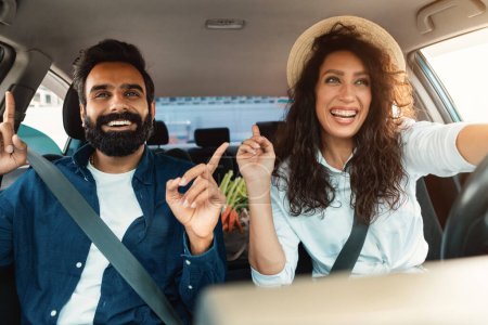 Photo for Go home after shopping. Cheerful arab couple driving in car with bag full of vegetables, listening to music and cherfully singing, shot from inside the auto - Royalty Free Image