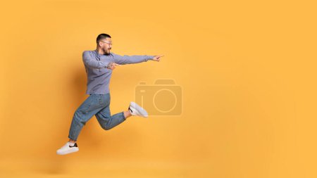 Téléchargez les photos : Super offre. Positif asiatique gars saut dans l'air et pointant vers l'espace de copie sur fond jaune, joyeux beau millénial homme démontrant place libre pour la publicité, panorama - en image libre de droit