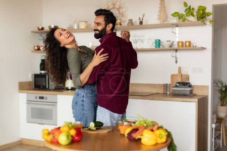 Photo for Excited arab spouses dancing together at kitchen and laughing, happy handsome man having romantic evening with his beautiful wife at home. Relationship, marriage, family concept - Royalty Free Image