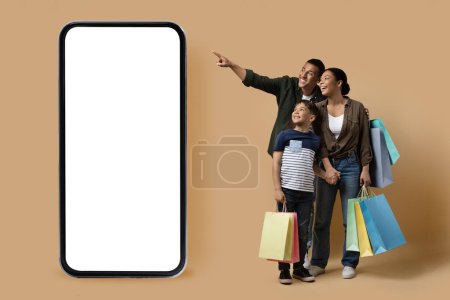 Photo for Cheerful happy loving black family father, mother and son child shopping online together isolated on beige background, big phone with white blank screen, mockup. Online offer, e-commerce - Royalty Free Image
