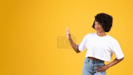 Foto de Mujer negra milenaria insatisfecha en gesto casual haciendo stop con la mano, aislada sobre fondo de estudio naranja, panorama. Espacio personal, emociones humanas, estilo de vida y decir no - Imagen libre de derechos
