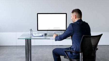Foto de Empresario en traje formal sentado en la mesa frente a la computadora con pantalla en blanco, maqueta para el diseño de sitios web de negocios. Hombre empleado que ofrece espacio libre para su anuncio en línea - Imagen libre de derechos