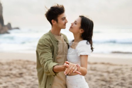 Téléchargez les photos : Jeune couple fiancé dansant et profitant d'une journée de fiançailles romantiques sur la plage, ayant un moment tendre sur la côte, se concentrer sur les mains - en image libre de droit