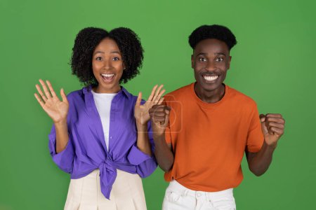 Téléchargez les photos : Heureux choqué jeune femme afro-américaine et homme décontracté à la bouche ouverte célébrant la victoire, le succès, isolé sur fond de studio vert. Surprise, bonnes nouvelles, relation, amour et vente - en image libre de droit