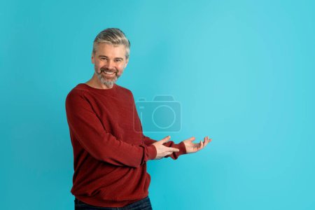 Photo for Great offer. Happy cheerful laughing handsome grey-haired middle aged man wearing casual outfit showing copy space for text or advertisement, isolated on blue studio background - Royalty Free Image