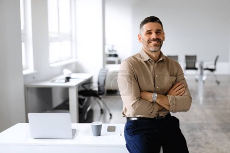Successful businessman. Confident man in shirt sitting on desk, posing with folded arms, looking and smiling at camera, copy space, place for advertisement