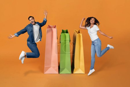 Photo for Shopaholics. Joyful Middle Eastern Spouses Celebrating Great Shopping, Jumping Near Huge Bags Smiling At Camera On Orange Background, Collage. Buyers Couple Advertising Sale Offer Near Shoppers - Royalty Free Image