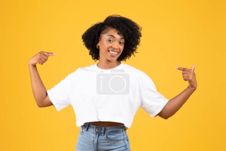 Téléchargez les photos : Heureuse fière femme noire millénaire confiante aux doigts pointant vers elle-même, isolée sur fond de studio orange. Émotions humaines, victoire, confiance en soi, publicité et offre, victoire - en image libre de droit