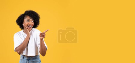 Téléchargez les photos : Joyeux choqué jeune femme noire décontractée à bouche ouverte, pointeur vers l'espace de copie, isolé sur fond de studio orange, panorama. Vente énorme, réaction surprise, émotions humaines, annonce et offre - en image libre de droit