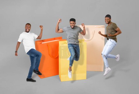 Photo for Sale Offer Approval. Three Emotional African American Guys Near Huge Shopping Bags Jumping And Gesturing Yes Over Gray Studio Background. Commerce And Consumerism. Collage, Full Length Shot - Royalty Free Image