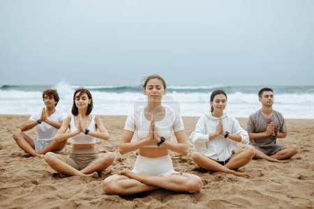 Téléchargez les photos : Méditation sur la plage. Femmes et hommes pratiquant le yoga sur la plage, amis zen assis en position lotus, tenant la main en namaste, faisant des exercices de respiration à la côte - en image libre de droit
