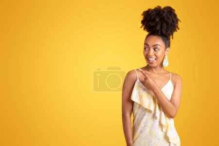 Foto de Sonriente dama afroamericana milenaria apuntando con el dedo al espacio vacío, aislada sobre fondo amarillo, estudio. Recomendación venta, anuncio y oferta, buenas noticias, estilo de vida - Imagen libre de derechos