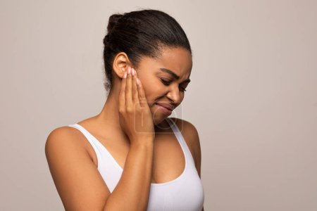 Photo for Tinnitus. Profile studio shot of sick young african american woman in white top having ear pain, touching her painful head, copy space, isolated on grey background - Royalty Free Image