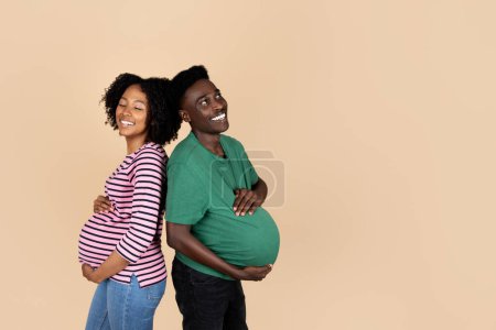 Téléchargez les photos : Amusez-vous bien ensemble, mari afro-américain millénaire joyeux et dame au gros ventre, isolé sur fond beige, studio. Relations familiales, attente de l'enfant, enceinte - en image libre de droit